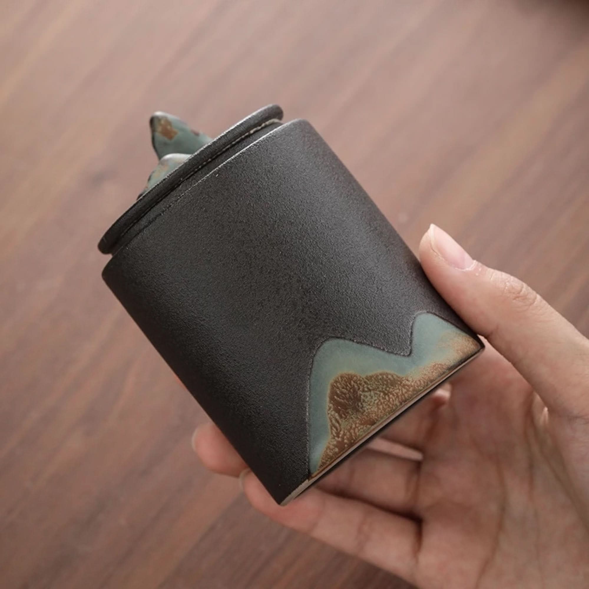 Matte finish ceramic tea canister in dark gray with earthy green and brown accents. Home decor.